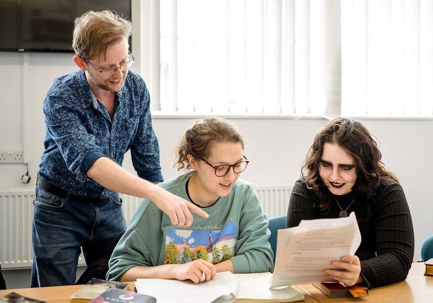 English Literature students reading a book together with their tutor behind them.