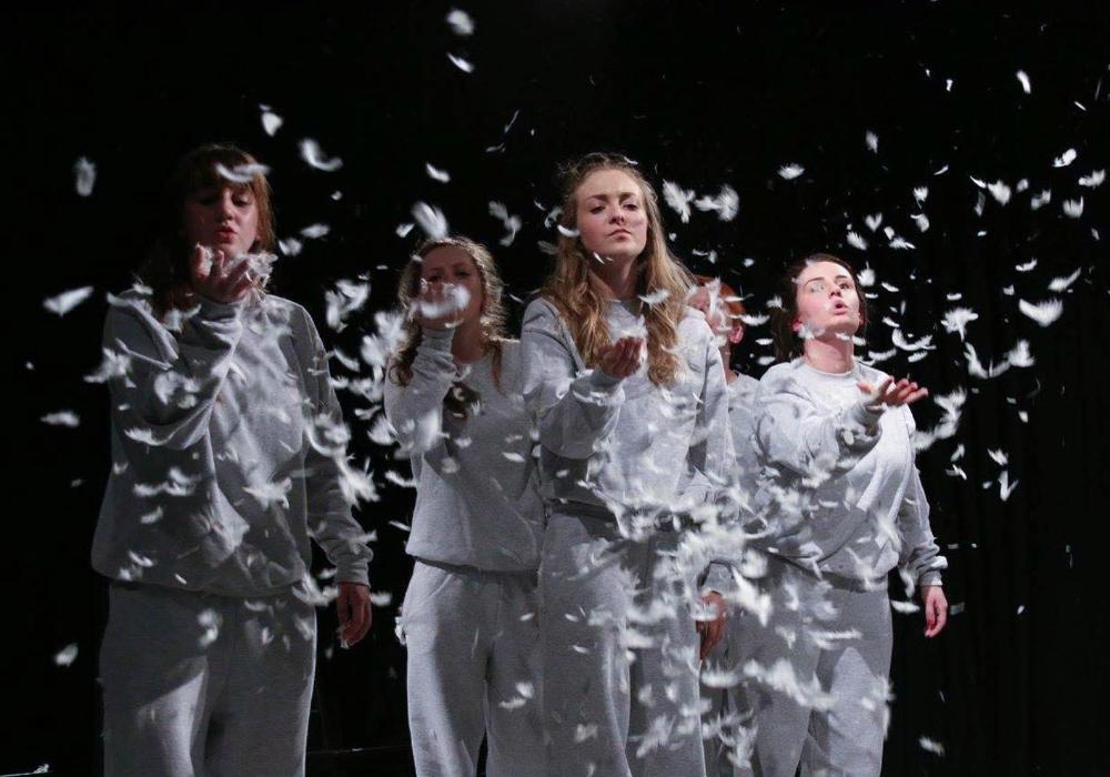 Students dressed in grey blowing feathers.