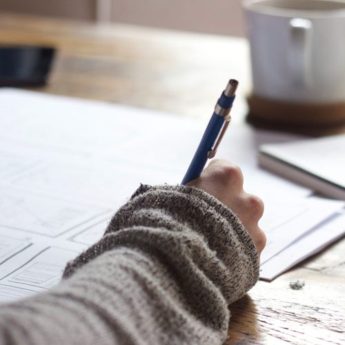 A student studying. They are writing with a black pen in their hand. 